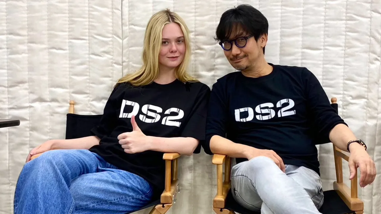 Elle Fanning e Hideo Kojima seduti su due sedie con magliette DS2 durante la promozione di Death Stranding 2